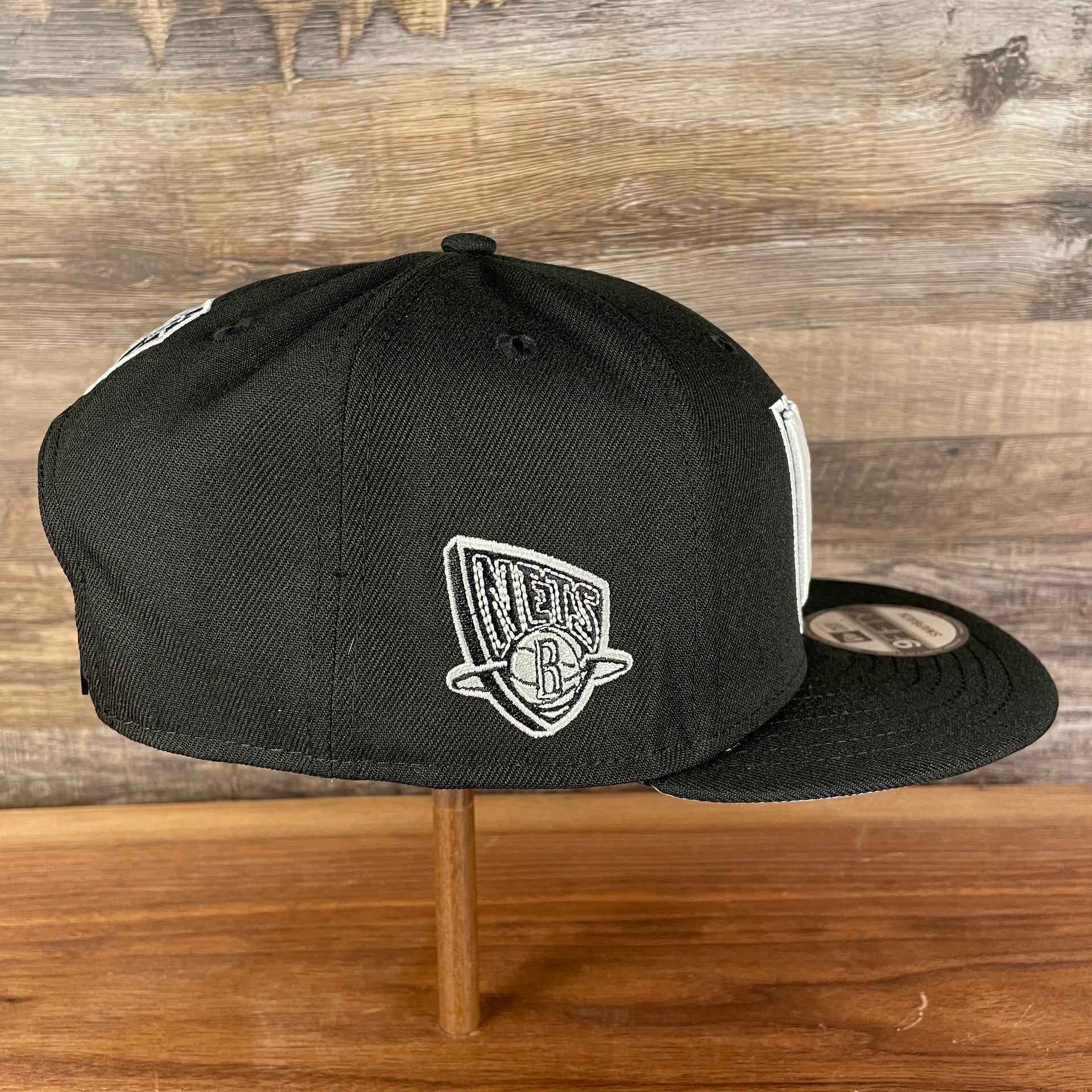 Wearer's right of the Brooklyn Nets NBA 75th Anniversary 2012 Side Patch Gray Bottom Black 9Fifty Snapback Hat | City Edition