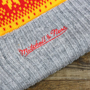 The Mitchell And Ness Script Logo on the Retro Houston Rockets Arctic Snowflake Ugly Sweater Pattern Cuffed Beanie With Pom Pom | Yellow, Maroon, and Gray Winter Beanie