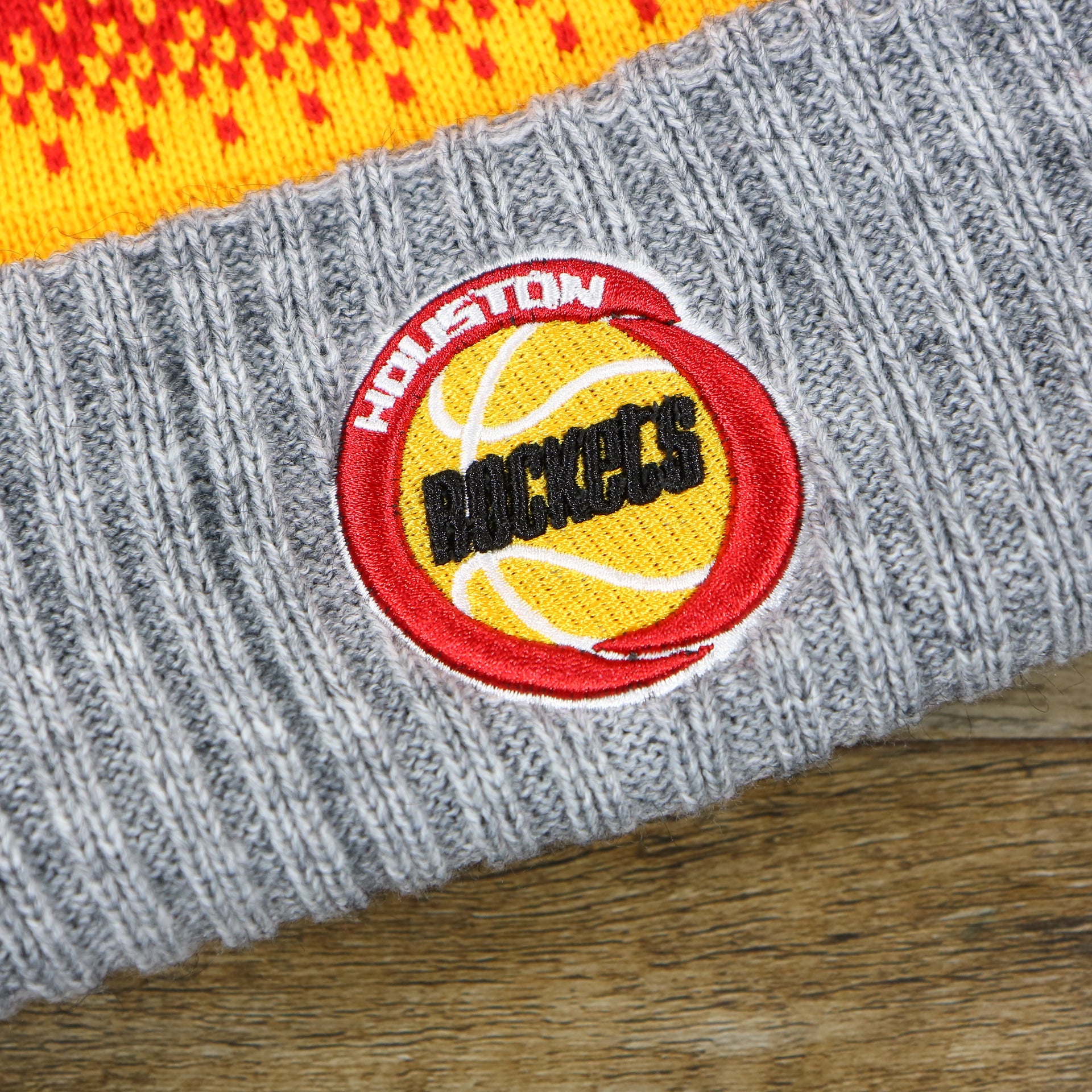 the Houston Rockets Logo on the Retro Houston Rockets Arctic Snowflake Ugly Sweater Pattern Cuffed Beanie With Pom Pom | Yellow, Maroon, and Gray Winter Beanie