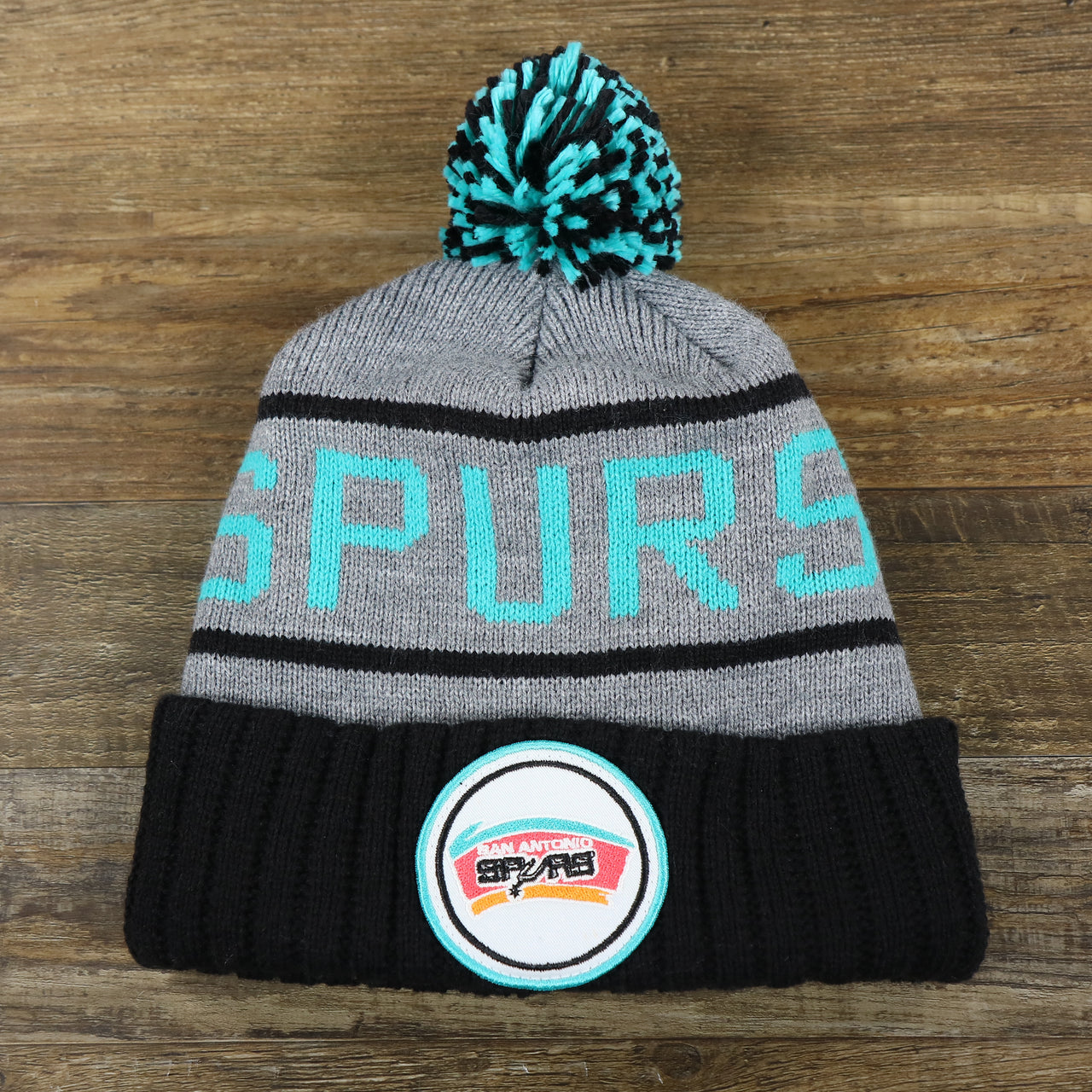 The front of the Retro San Antonio Spurs Striped Wordmark Cuffed Pom Pom Beanie | Gray And Black Winter Beanie