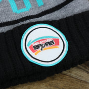 The San Antonio Spurs retro Logo on the Retro San Antonio Spurs Striped Wordmark Cuffed Pom Pom Beanie | Gray And Black Winter Beanie