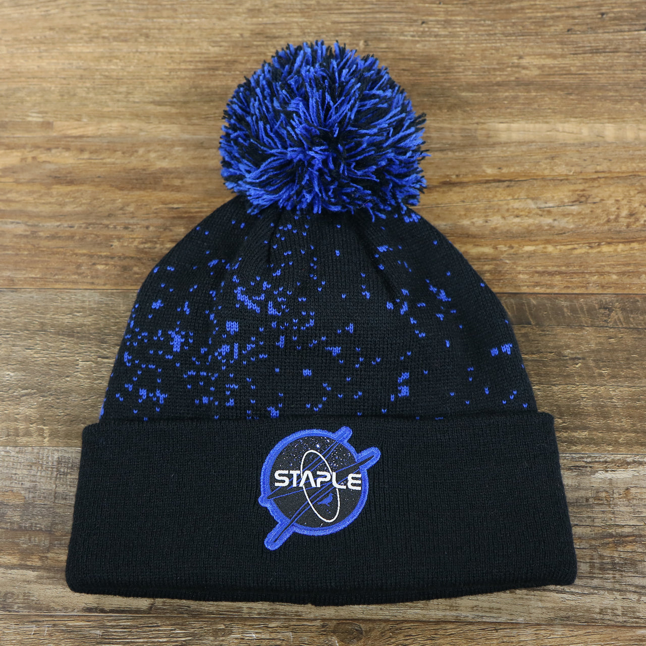 The front of the Staple Space Logo Space Print Cuffed Pom Pom Winter Beanie | Black And Royal Blue Beanie