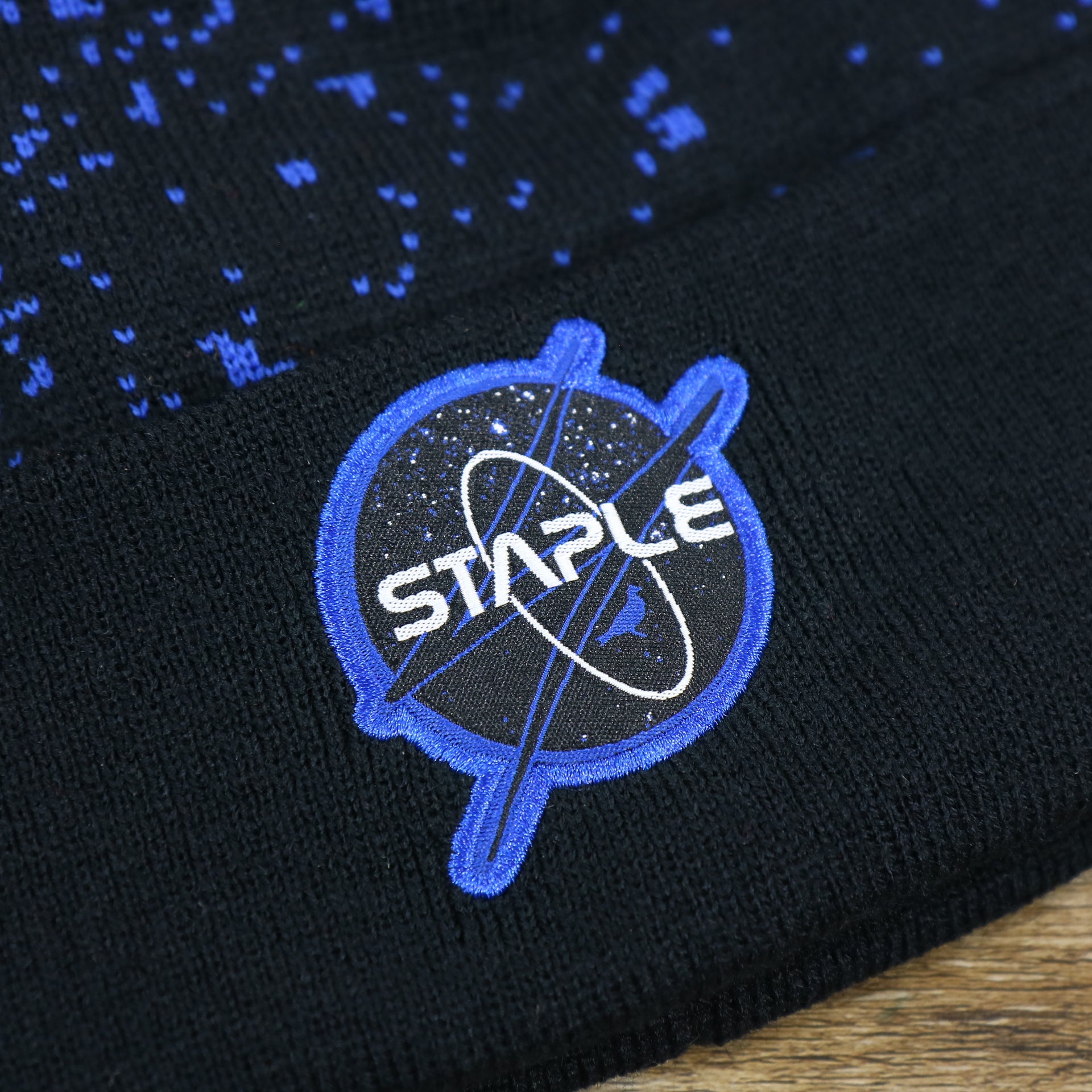 The Staple Space Logo on the Staple Space Logo Space Print Cuffed Pom Pom Winter Beanie | Black And Royal Blue Beanie