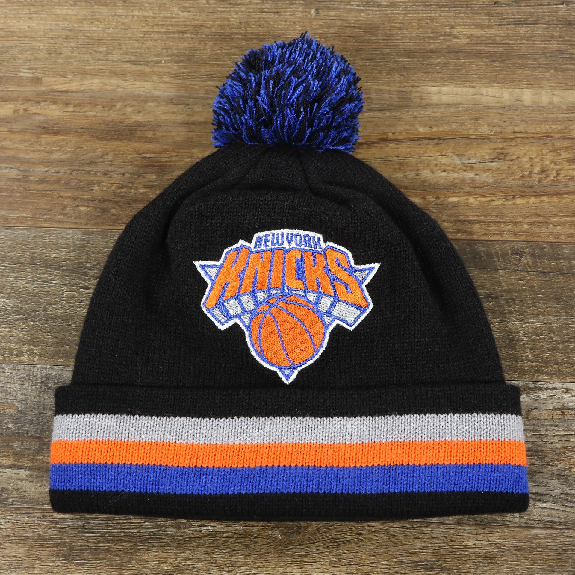 The front of the New York Knicks Striped Cuff Black Out Blackout Knit WInter Beanie With Multi Colored Pom Pom | Black Winter Beanie
