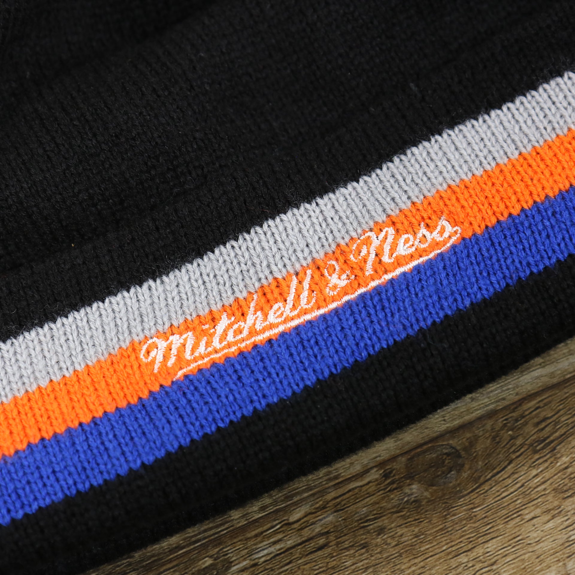 The Mitchell And Ness Script Logo on the New York Knicks Striped Cuff Black Out Blackout Knit WInter Beanie With Multi Colored Pom Pom | Black Winter Beanie