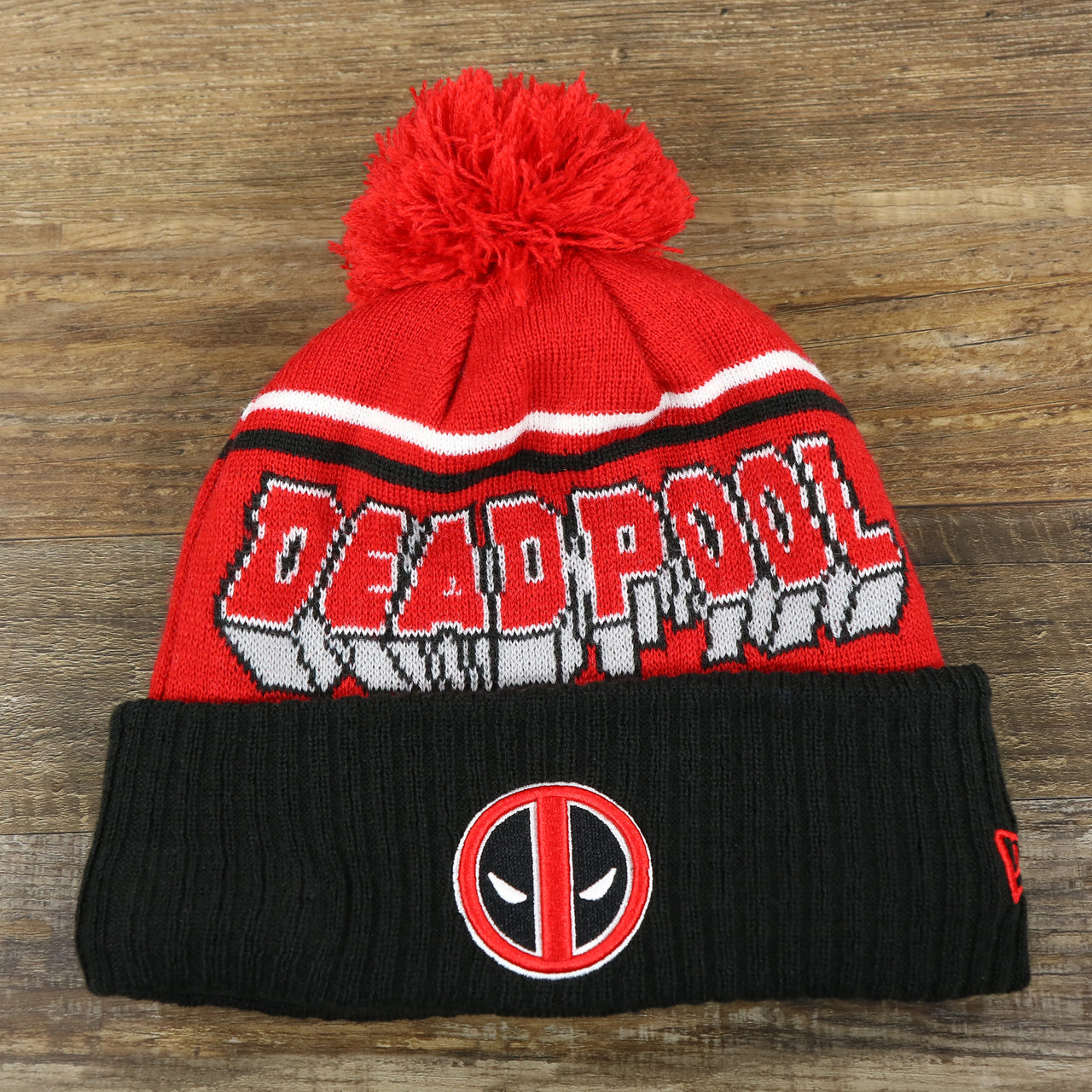 The front of the DC Comics Deadpool Mask Logo Deadpool Wordmark Striped Beanie With Red Pom Pom | Red And Black Winter Beanie