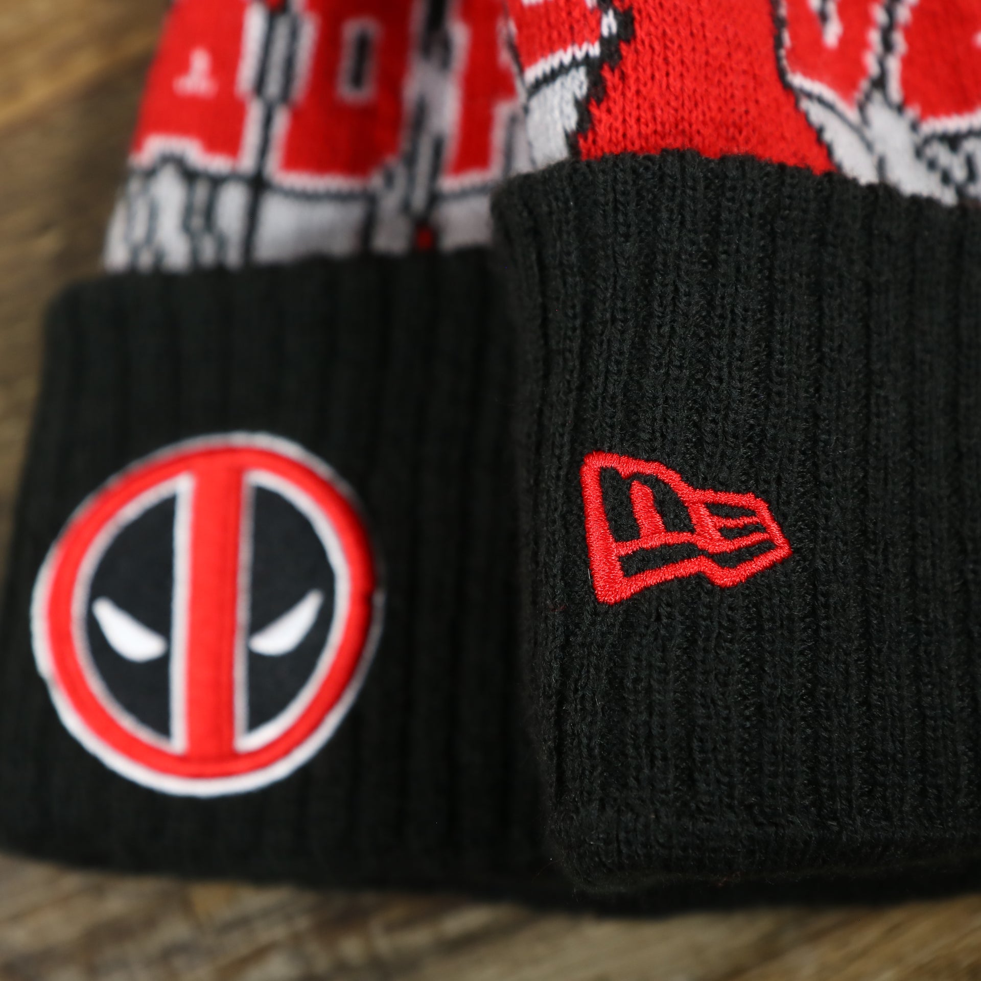 The New Era Logo on the DC Comics Deadpool Mask Logo Deadpool Wordmark Striped Beanie With Red Pom Pom | Red And Black Winter Beanie