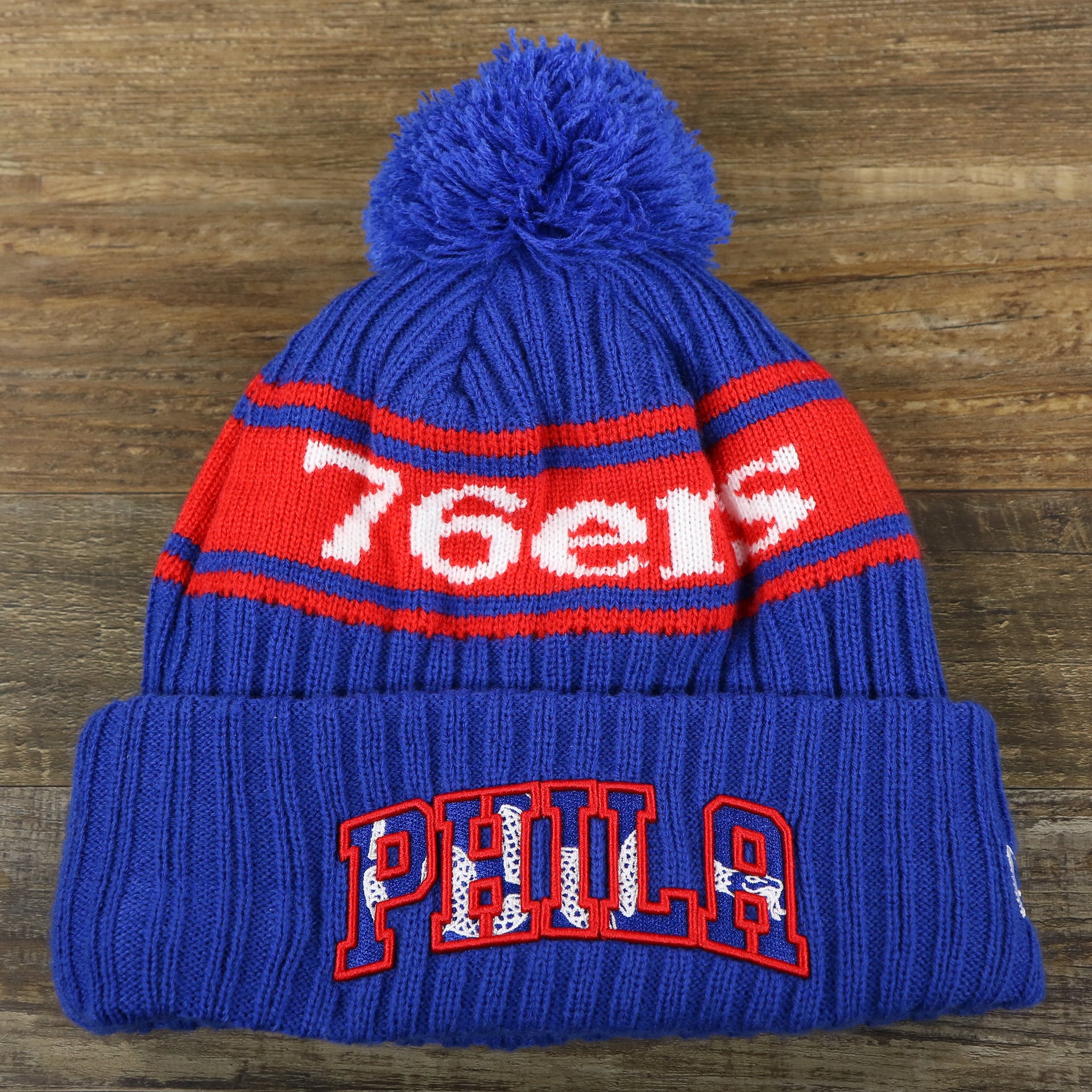 The front of the Philadelphia 76ers Knit Wordmark Phila Arch Lettering Join Or Die Snake NBA Draft Striped Beanie | Royal Blue and Red Beanie