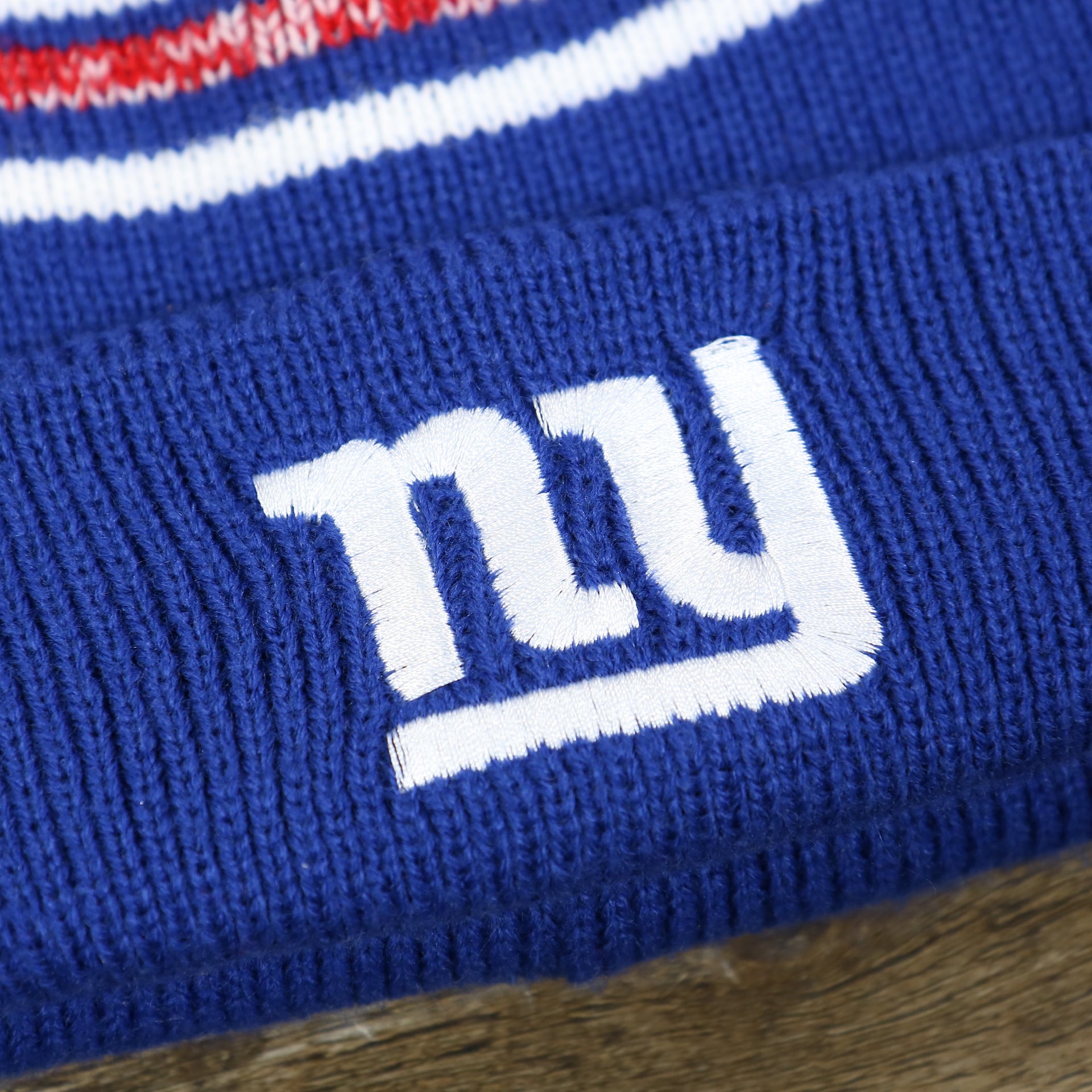 The Giants Logo on the Kid’s New York Giants Striped Pom Pom Winter Beanie | Royal Blue, Red, And White Beanie