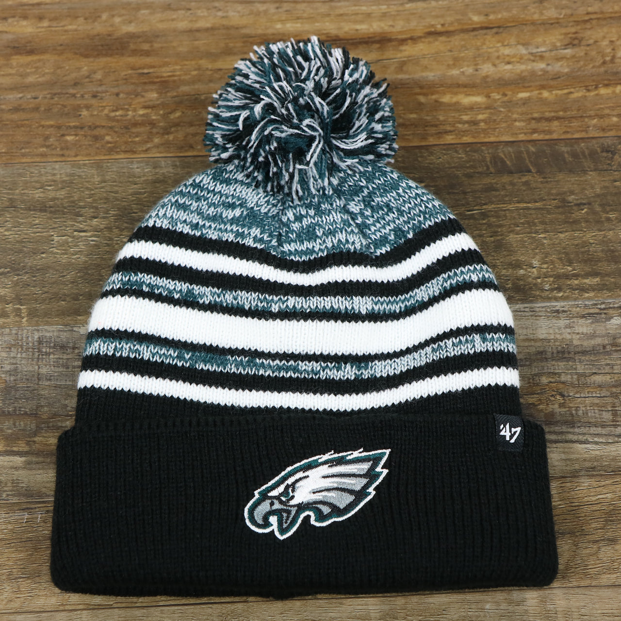 The front of the Kid’s Philadelphia Eagles Striped Pom Pom Winter Beanie | Black, Midnight Green, And White Beanie