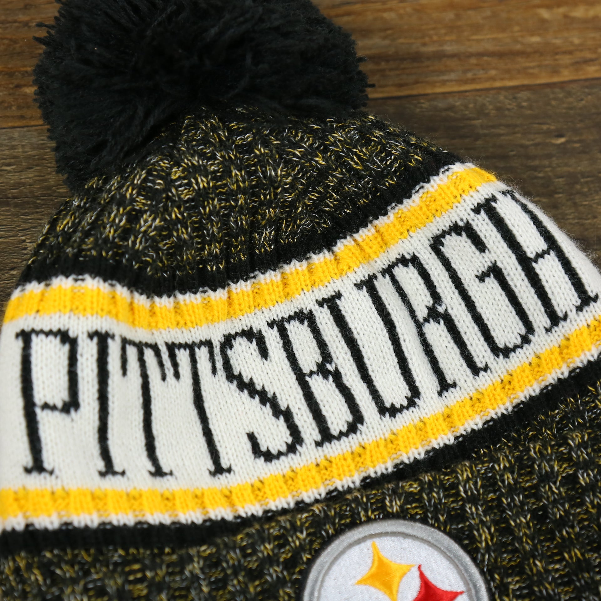 The Pittsburgh Steelers Logo on the Pittsburgh Steelers On Field Cold Weather Striped Wordmark Pom Pom Winter Beanie | Black and Yellow Beanie