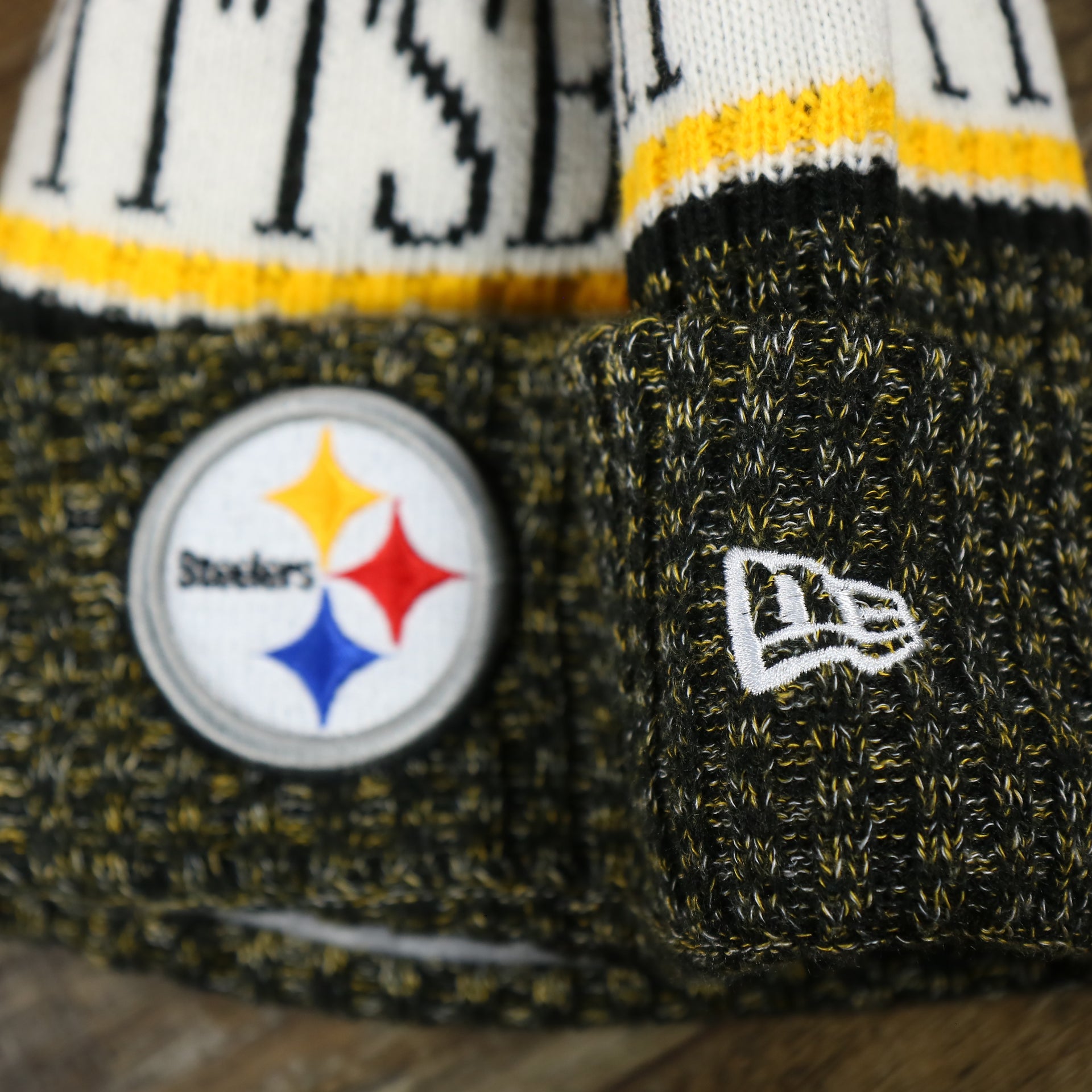 The New Era Logo on the Pittsburgh Steelers On Field Cold Weather Striped Wordmark Pom Pom Winter Beanie | Black and Yellow Beanie
