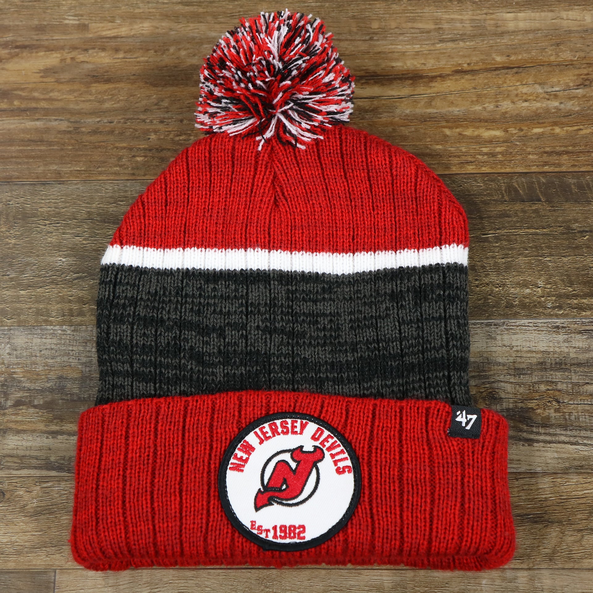 The front of the New Jersey Devils Cuffed Logo Striped Winter Beanie With Pom Pom | Red and Gray Winter Beanie