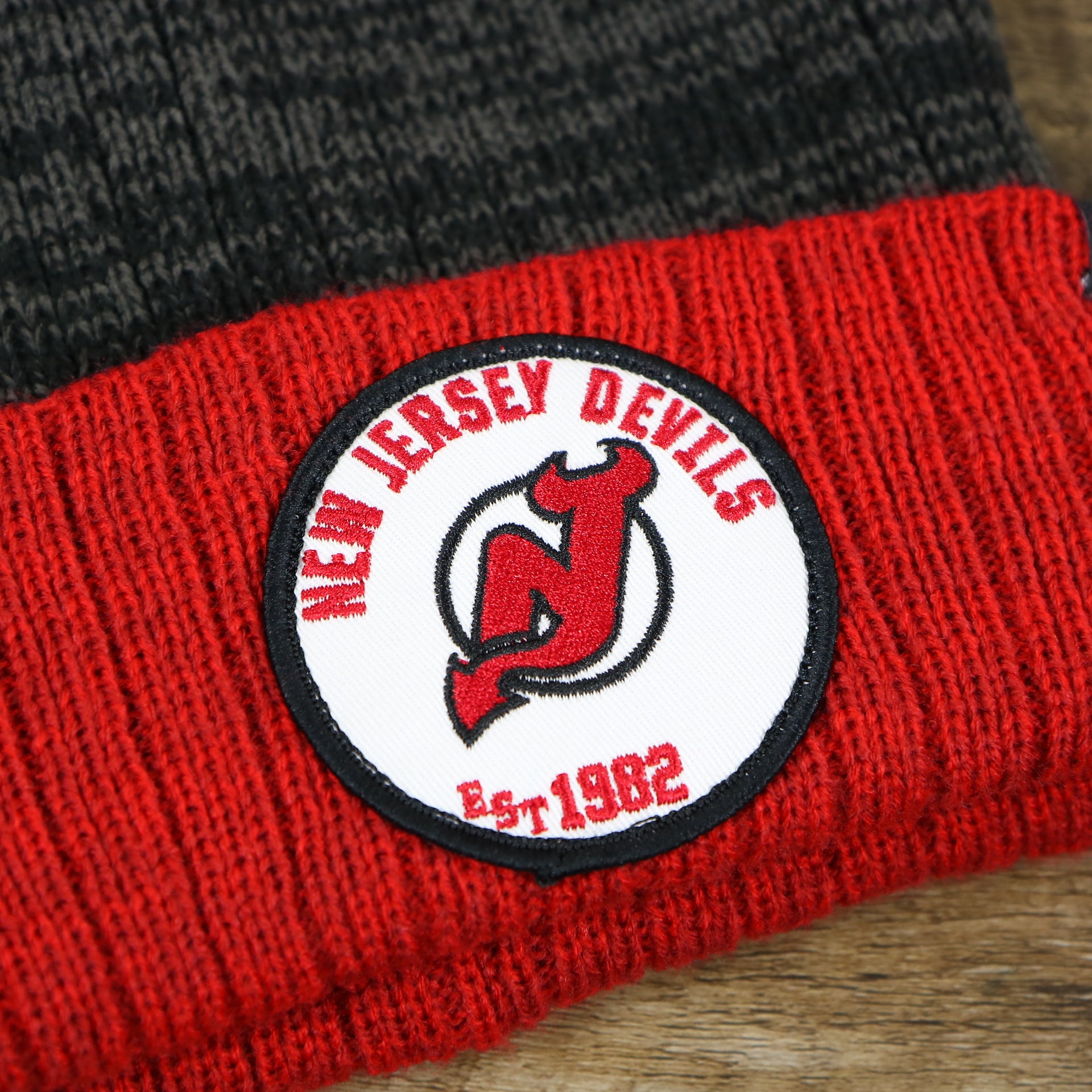 The New jersey Devils Logo on the New Jersey Devils Cuffed Logo Striped Winter Beanie With Pom Pom | Red and Gray Winter Beanie
