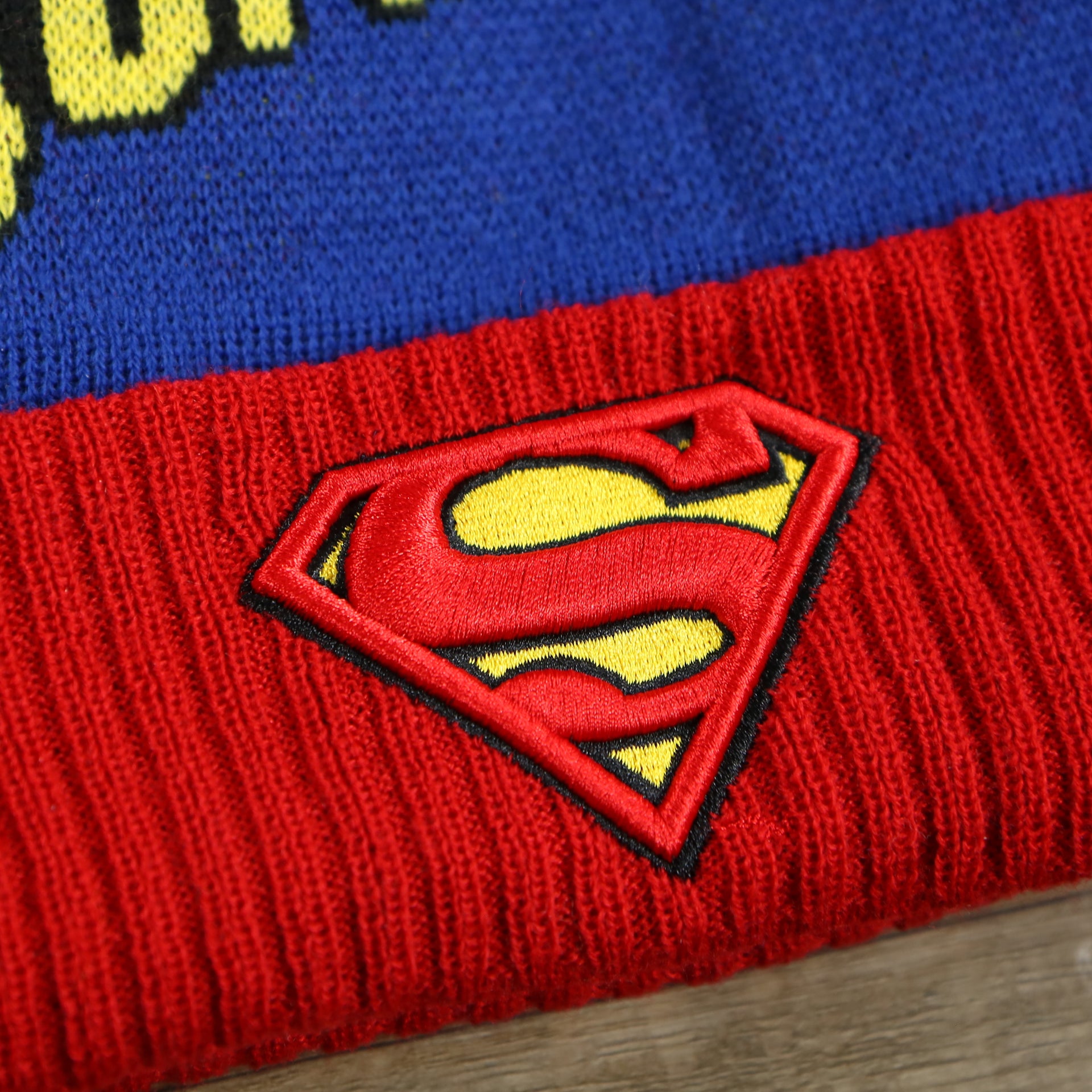 The Superman Logo on the DC Comics Superman S-Shield Logo Superman Wordmark Striped Beanie With Blue Pom Pom | Blue And Red Winter Beanie