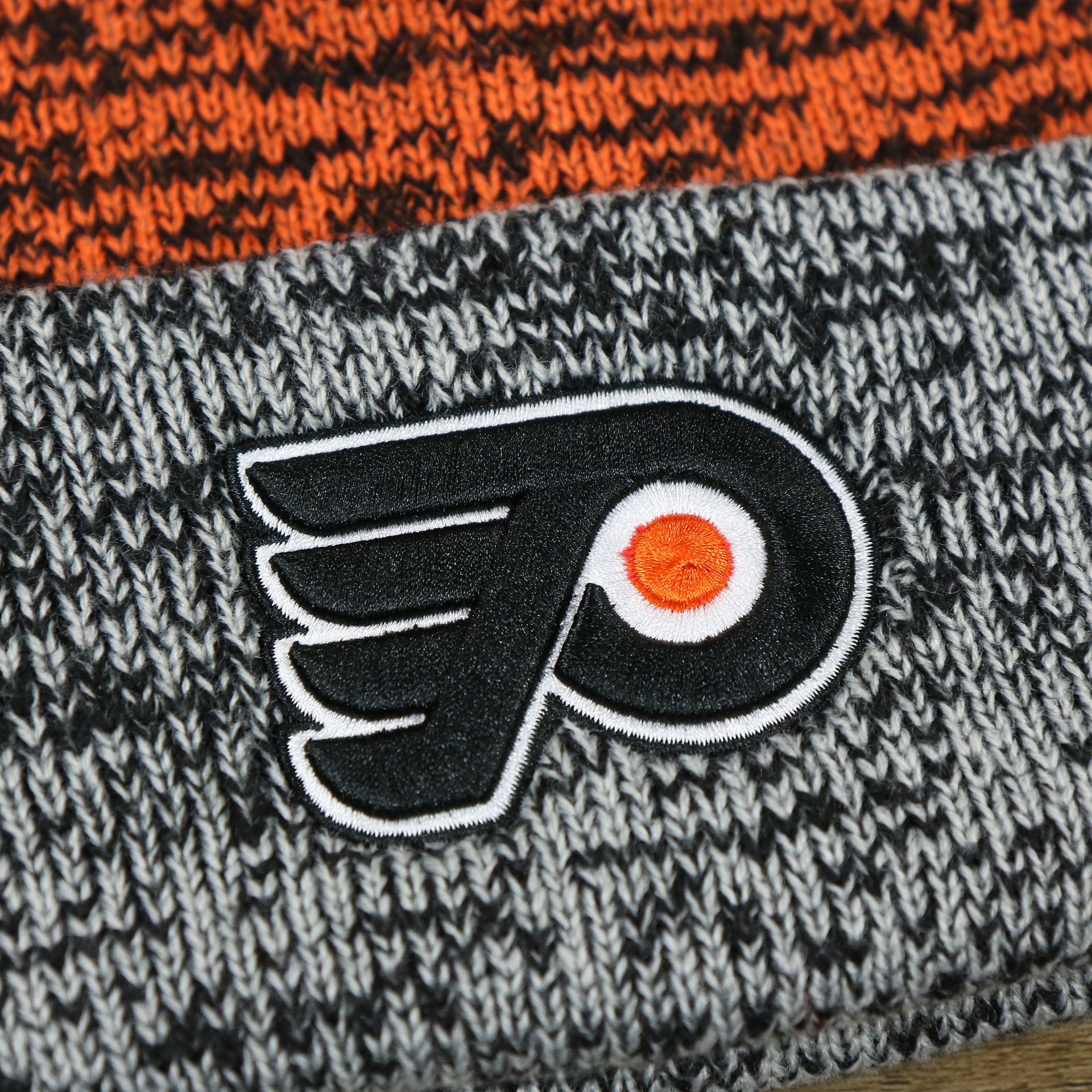 The Flyers Logo on the Philadelphia Flyers Static Knit Cuffed Winter Beanie With Pom Pom | Black, Orange, And Gray Beanie