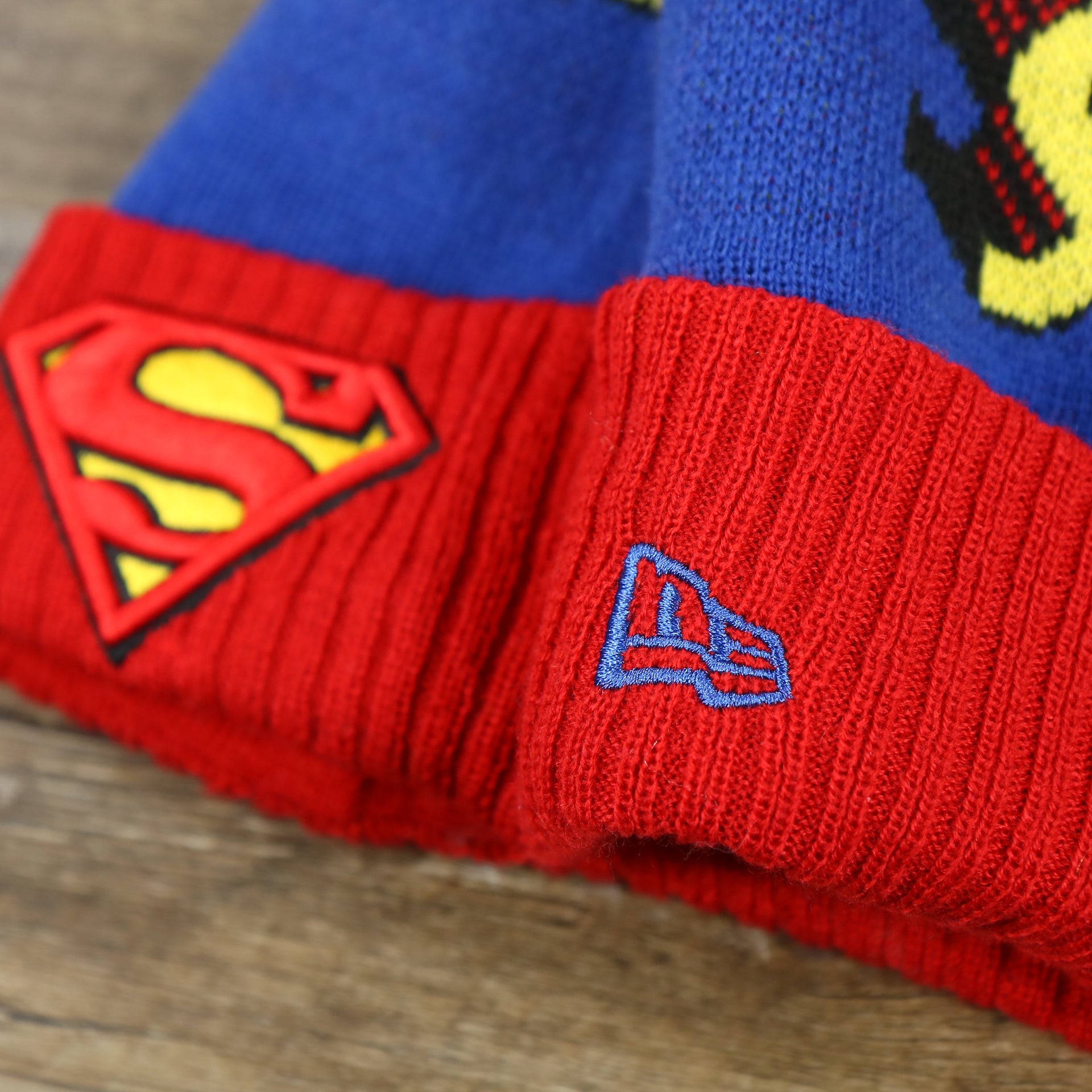 The New Era Logo on the DC Comics Superman S-Shield Logo Superman Wordmark Striped Beanie With Blue Pom Pom | Blue And Red Winter Beanie