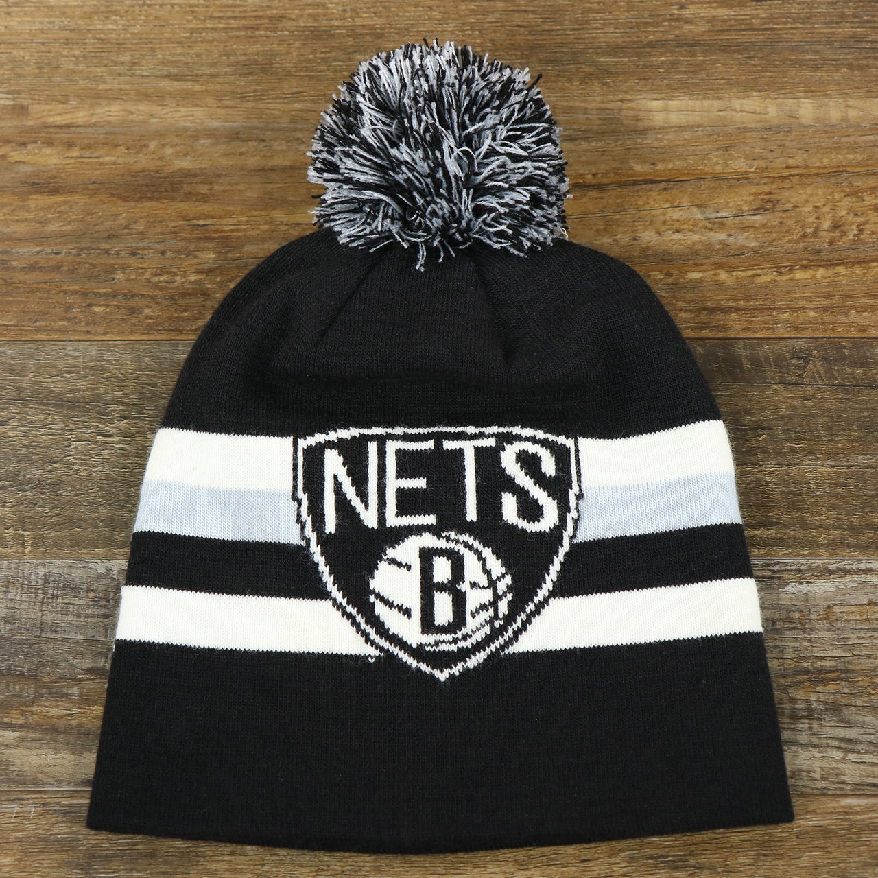 The front of the Brooklyn Nets Cuffless Striped Winter Beanie With Pom Pom | Black, White, And Gray Beanie