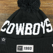 The Cowboys Wordmark on the Dallas Cowboys On Field Rubber Cowboys 1960 Patch Cuffed Pom Pom Winter Beanie | Black Winter Beanie