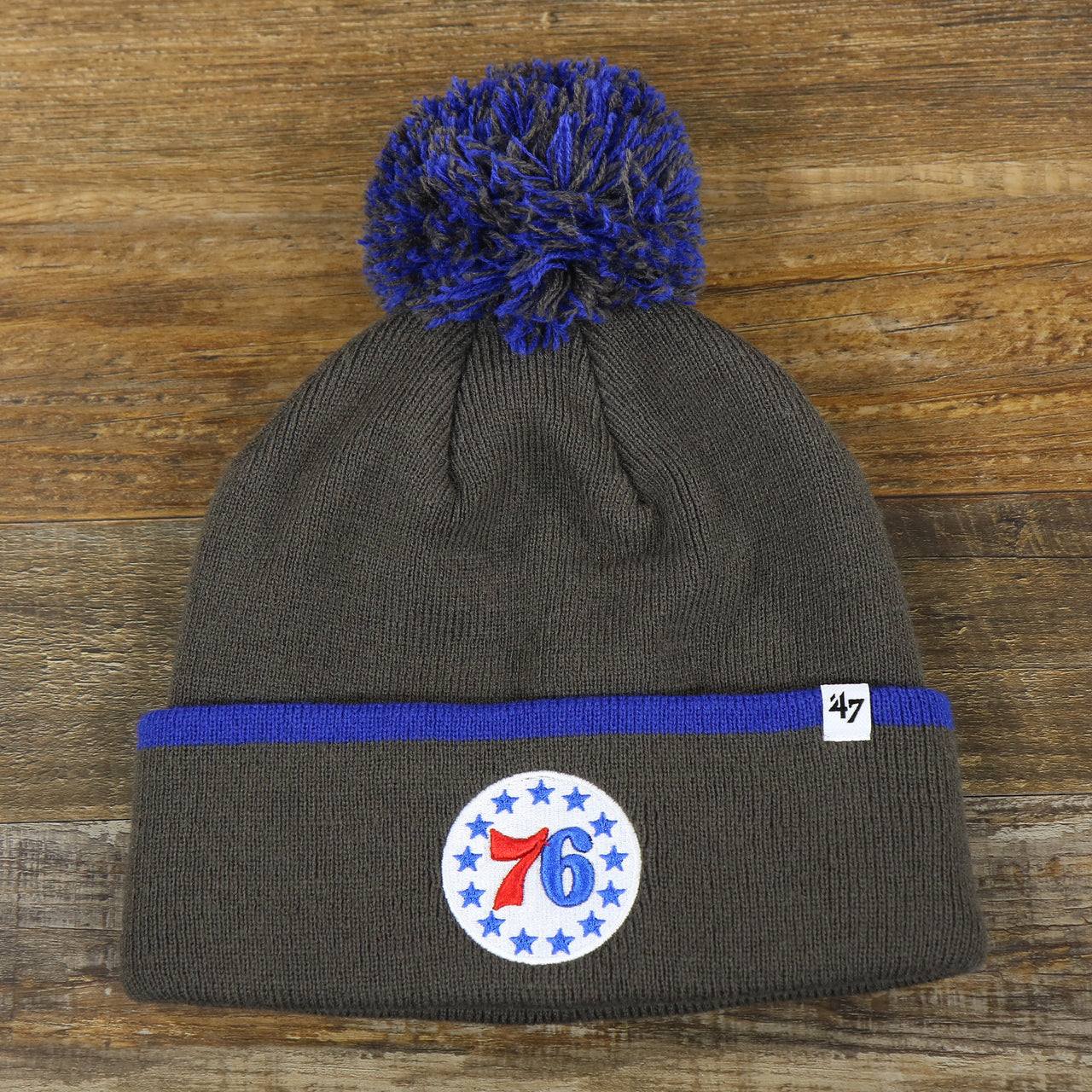 The front of the Philadelphia 76ers Cuffed Logo Baraka Knit Charcoal Winter Beanie | Gray And Royal Blue Beanie