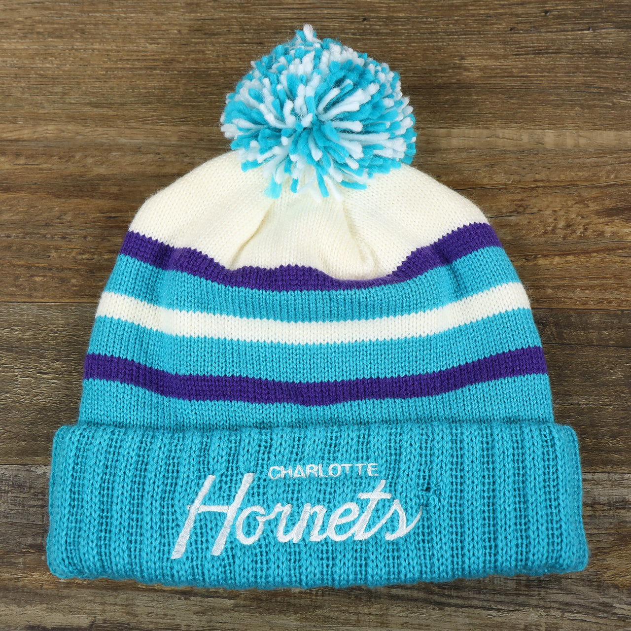 The front of the Charlotte Hornets Cursive Wordmark Teal Blue Cuff Pom Pom Winter Beanie | Teal Blue Striped Winter Beanie