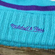 The Mitchell And Ness Script Logo on the Charlotte Hornets Cursive Wordmark Teal Blue Cuff Pom Pom Winter Beanie | Teal Blue Striped Winter Beanie
