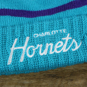 The Charlotte Hornets Wordmark on the Charlotte Hornets Cursive Wordmark Teal Blue Cuff Pom Pom Winter Beanie | Teal Blue Striped Winter Beanie