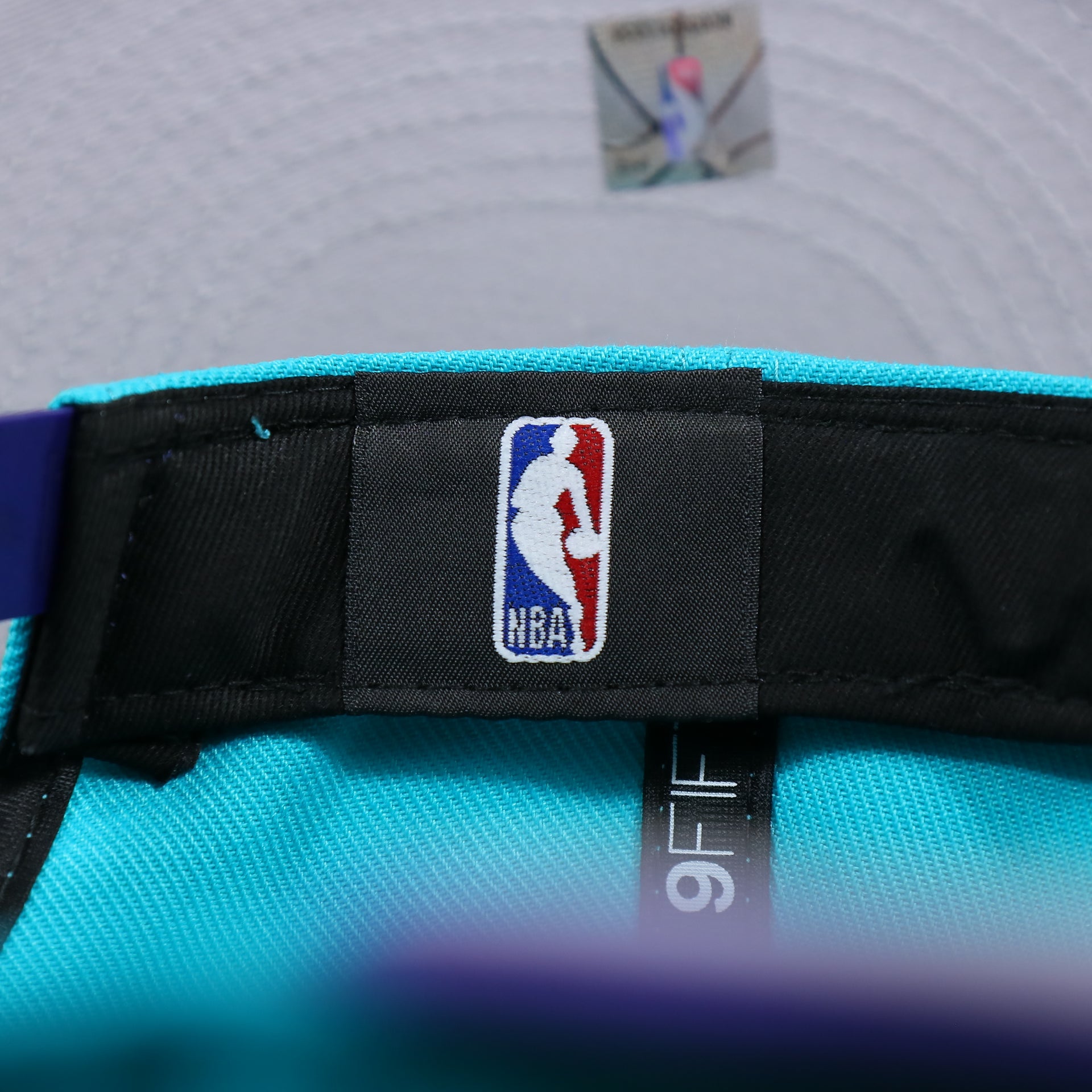 The NBA tag on the Charlotte Hornets Team Script Gray Bottom 9Fifty Snapback | Turquoise and Purple Snap Cap