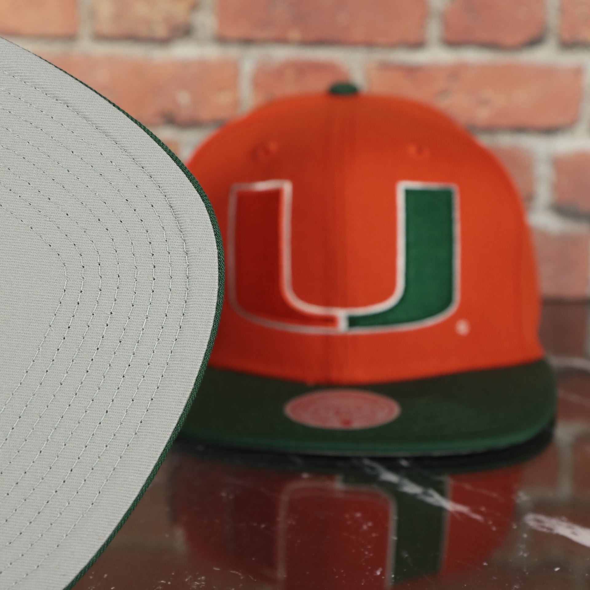 grey under visor on the Miami Hurricanes NCAA Jumbotron "U Miami" Ripped Wordmark side patch Grey Bottom Orange/Green Snapback hat | Mitchell and Ness Two Tone Snap Cap