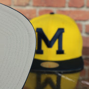 grey under visor on the Michigan Wolverines NCAA Jumbotron "Michigan" Ripped Wordmark side patch Grey Bottom Yellow/Navy Snapback hat | Mitchell and Ness Two Tone Snap Cap