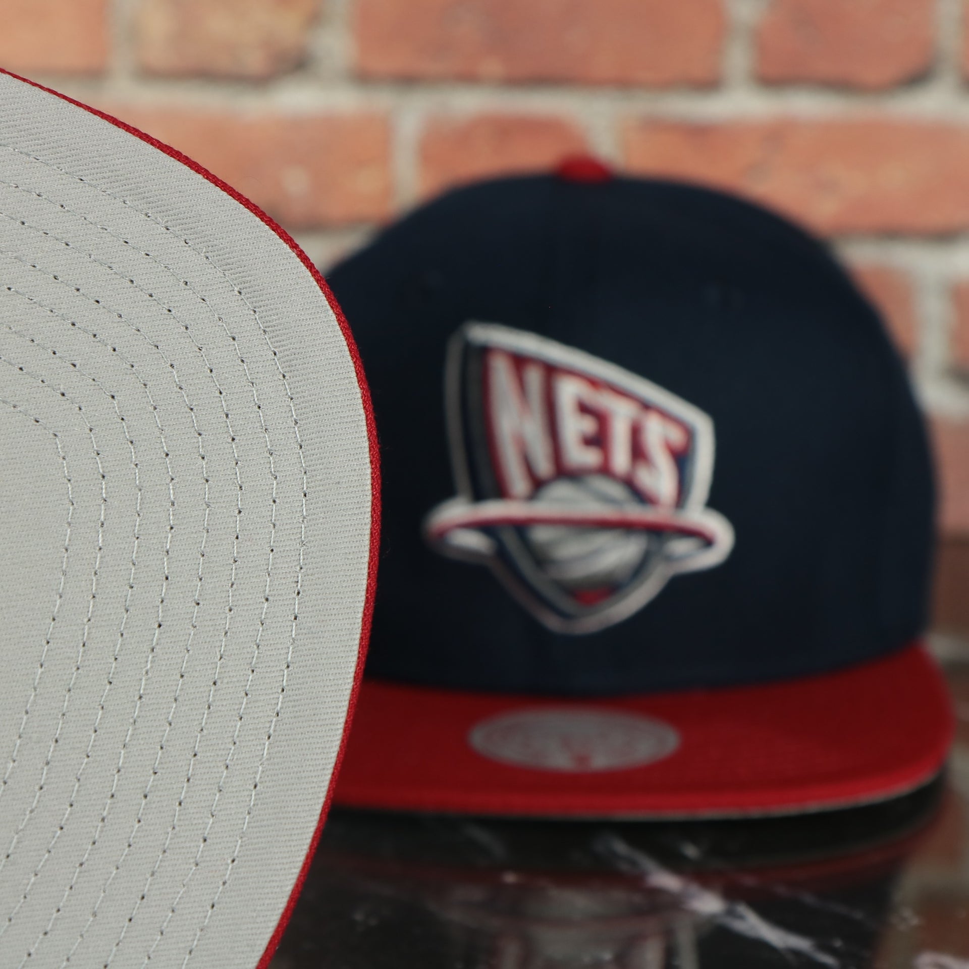 grey under visor on the New Jersey Nets Hardwood Classics Jumbotron "Nets" Ripped Wordmark side patch Grey Bottom Navy/Red Snapback hat | Mitchell and Ness Two Tone Snap Cap