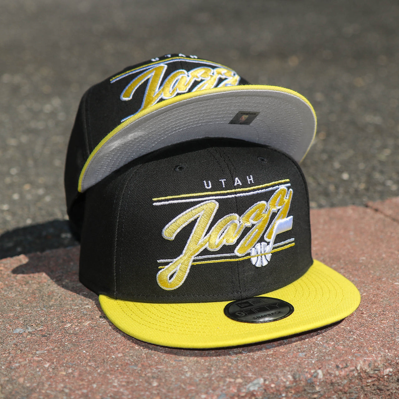 The front of the Utah Jazz Team Script Gray Bottom 9Fifty Snapback | Black and Yellow Snap Cap
