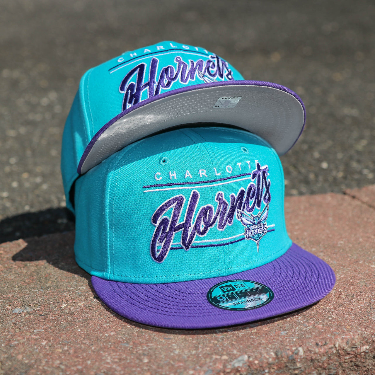The front of the Charlotte Hornets Team Script Gray Bottom 9Fifty Snapback | Turquoise and Purple Snap Cap