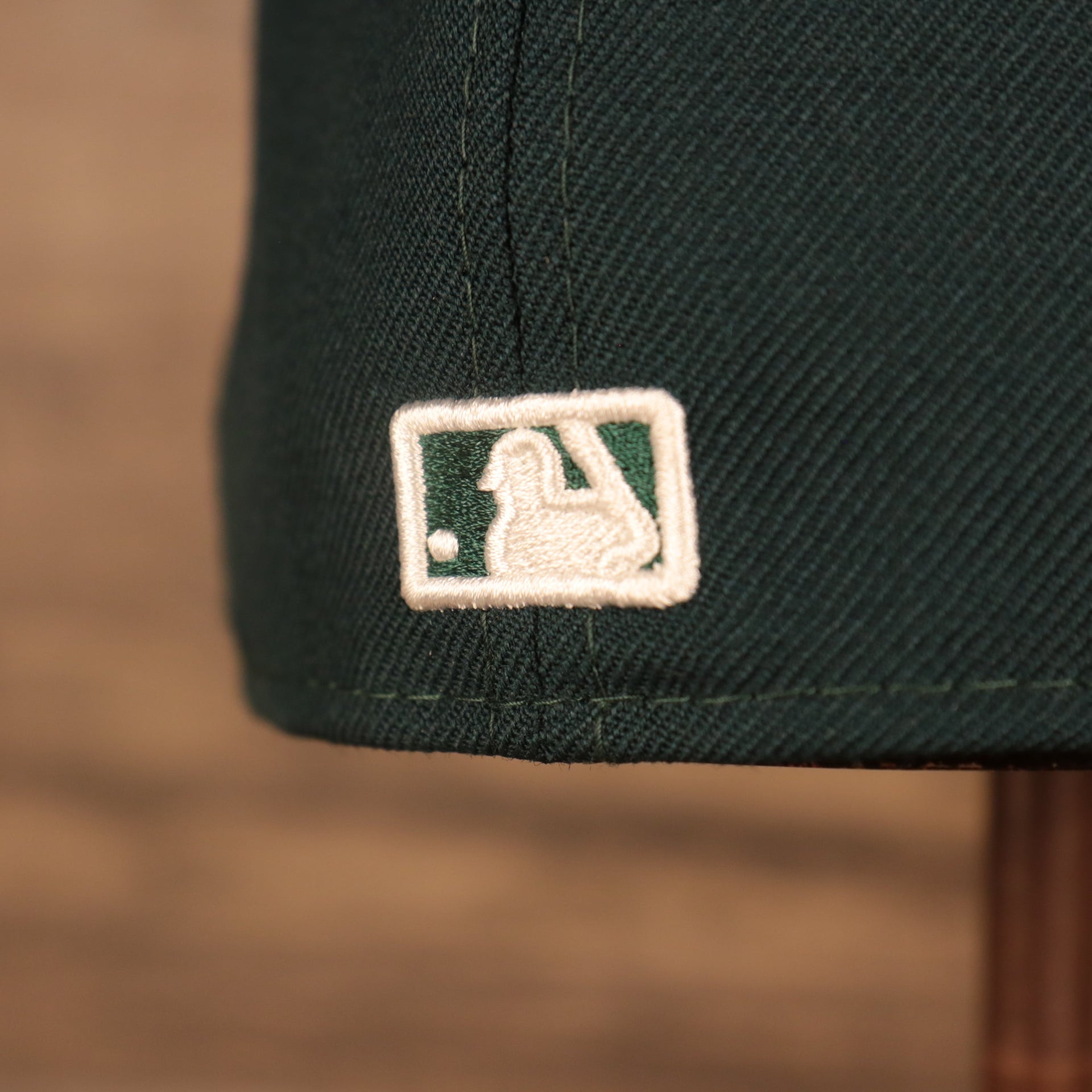 Close up of MLB logo on the back of Oakland Athletics Iced Out Side Patch Flower Oakland Bridge Gray Bottom 59Fifty Fitted Cap