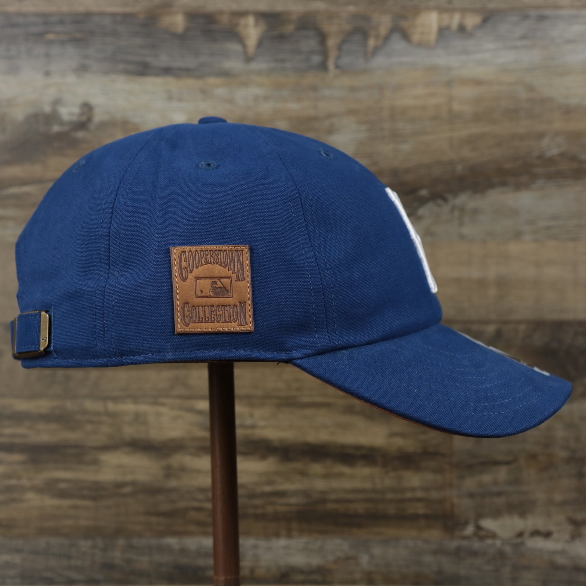 The wearer's right on the Cooperstown Brooklyn Dodgers Cooperstown Collection Side Patch Leather Brown Undervisor Dad Hat | Vintage Royal Blue Dad Hat