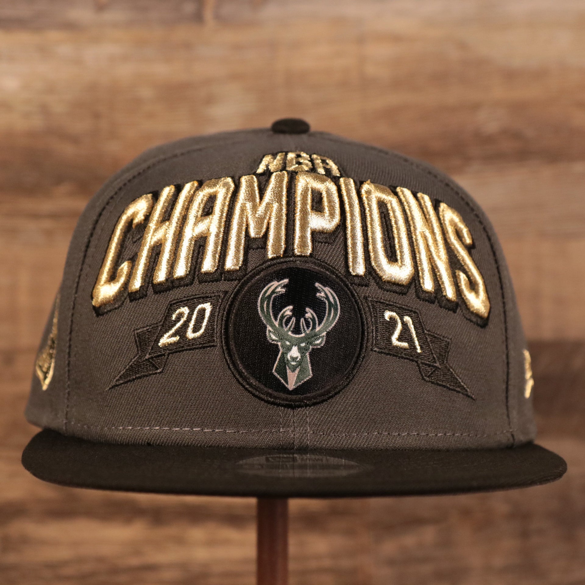 Embroidered on the front of the 2021 Milwaukee Bucks NBA Championship snapback hat is the lettering NBA Champions 2021 in metallic gold above the Milwaukee Bucks logo patch