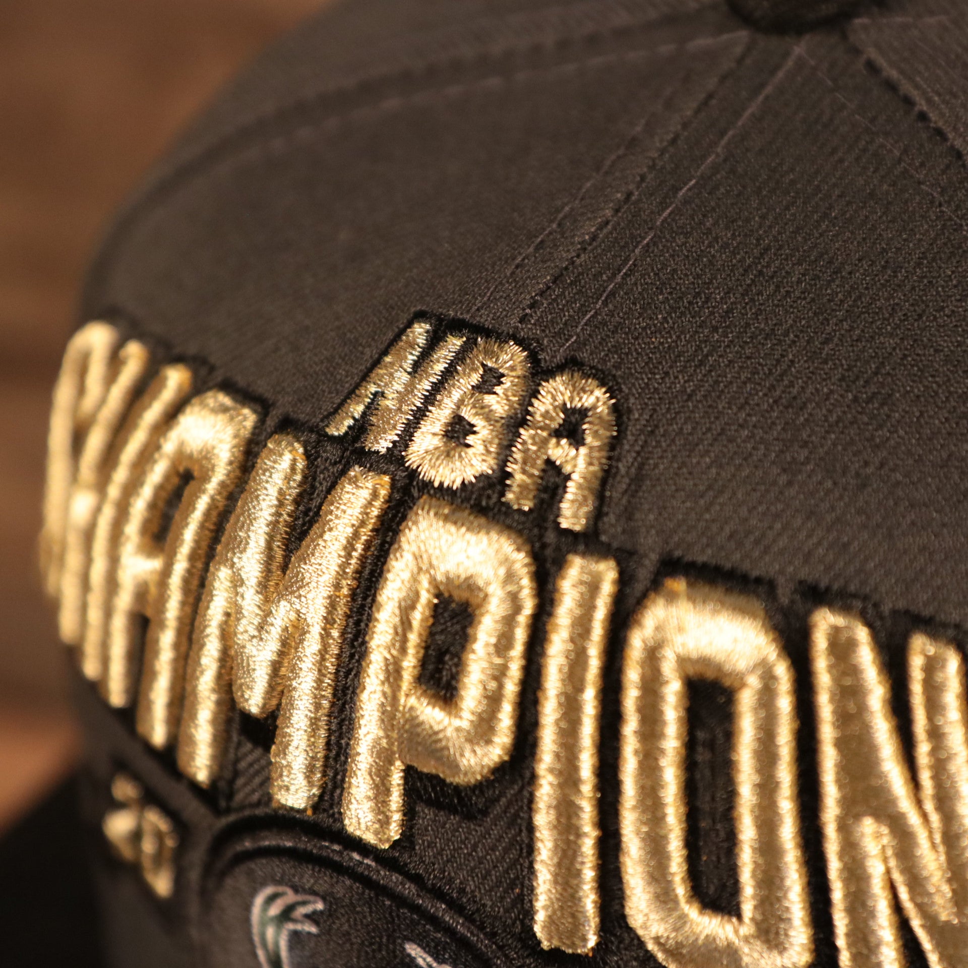 A close up of the NBA Champions embroidered in metallic gold on the front of the Milwaukee Bucks 2021 NBA Champions snapback hat