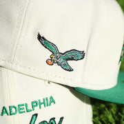 Close up of the throwback Eagles logo patch on the wearer's right of the Philadelphia Eagles Throwback Wordmark Jersey Script Cream/Kelly Green Black UV Side Patch 59Fifty Fitted Cap | Cap Swag Exclusive