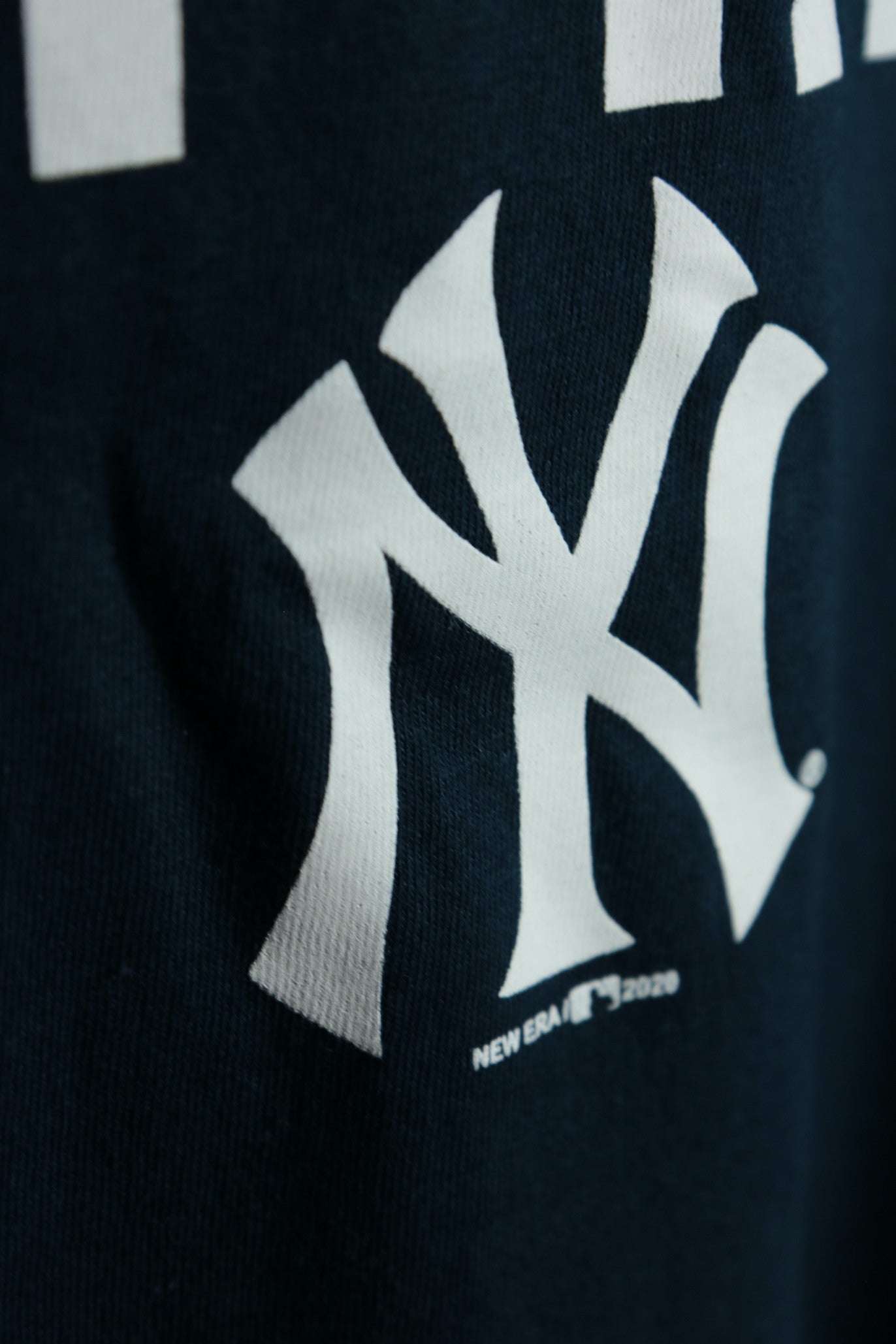 Close up of the Yankees logo on the front of New York Yankees The Captain 2020 Patch Hall of Fame Navy Blue Men's T-Shirt