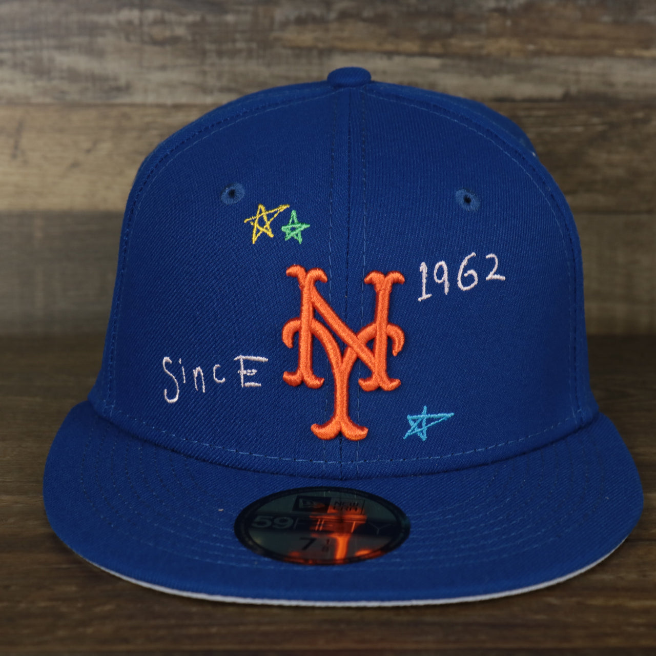 The front of the logo on the New York Mets “Scribble” Side Patch Gray Bottom 59Fifty Fitted Cap