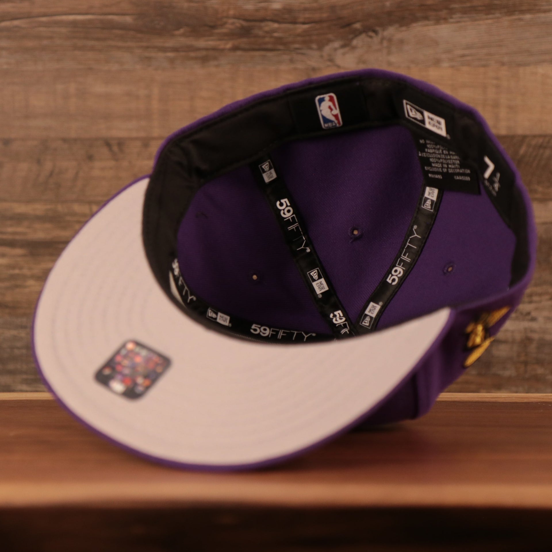The grey bottom brim of the purple Los Angeles Lakers all over embroidered 59fifty cap by New Era.