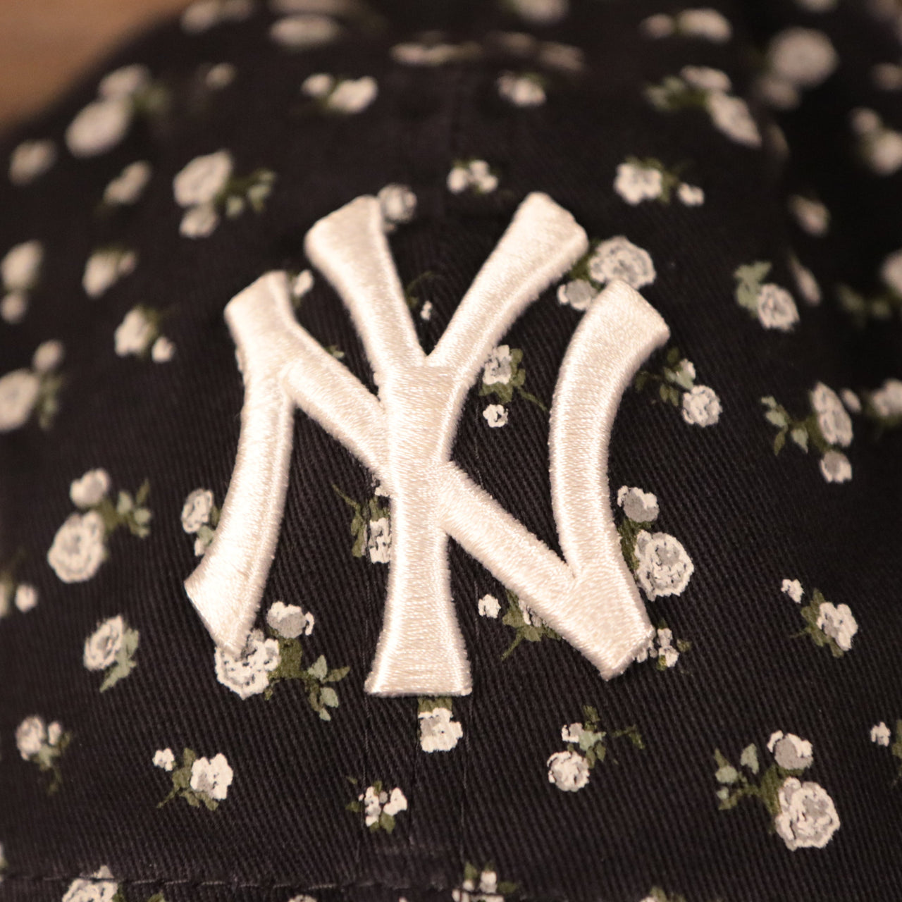 The white New York Yankees logo patch on the front side of the New Era floral baseball cap.