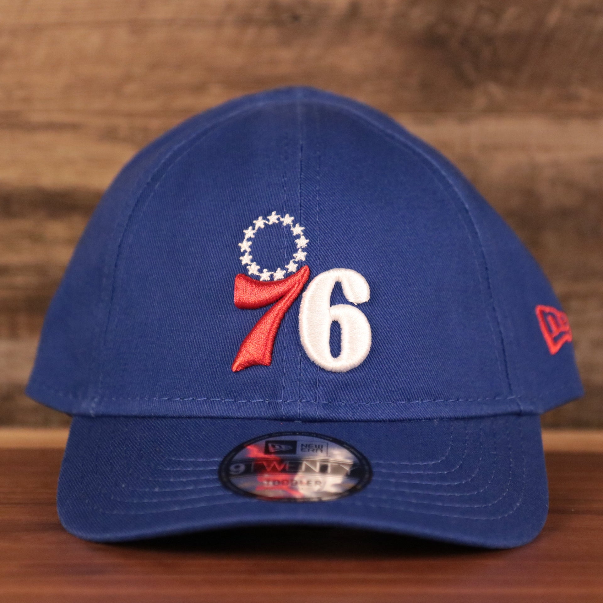 The front side logo of the Philadelphia 76ers on the royal blue New Era toddler ball cap.