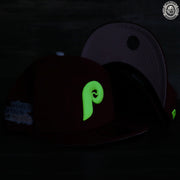 The green Philadelphia Phillies retro logo on the front side of the glow in the dark 59fifty fitted pink underbrim cap.