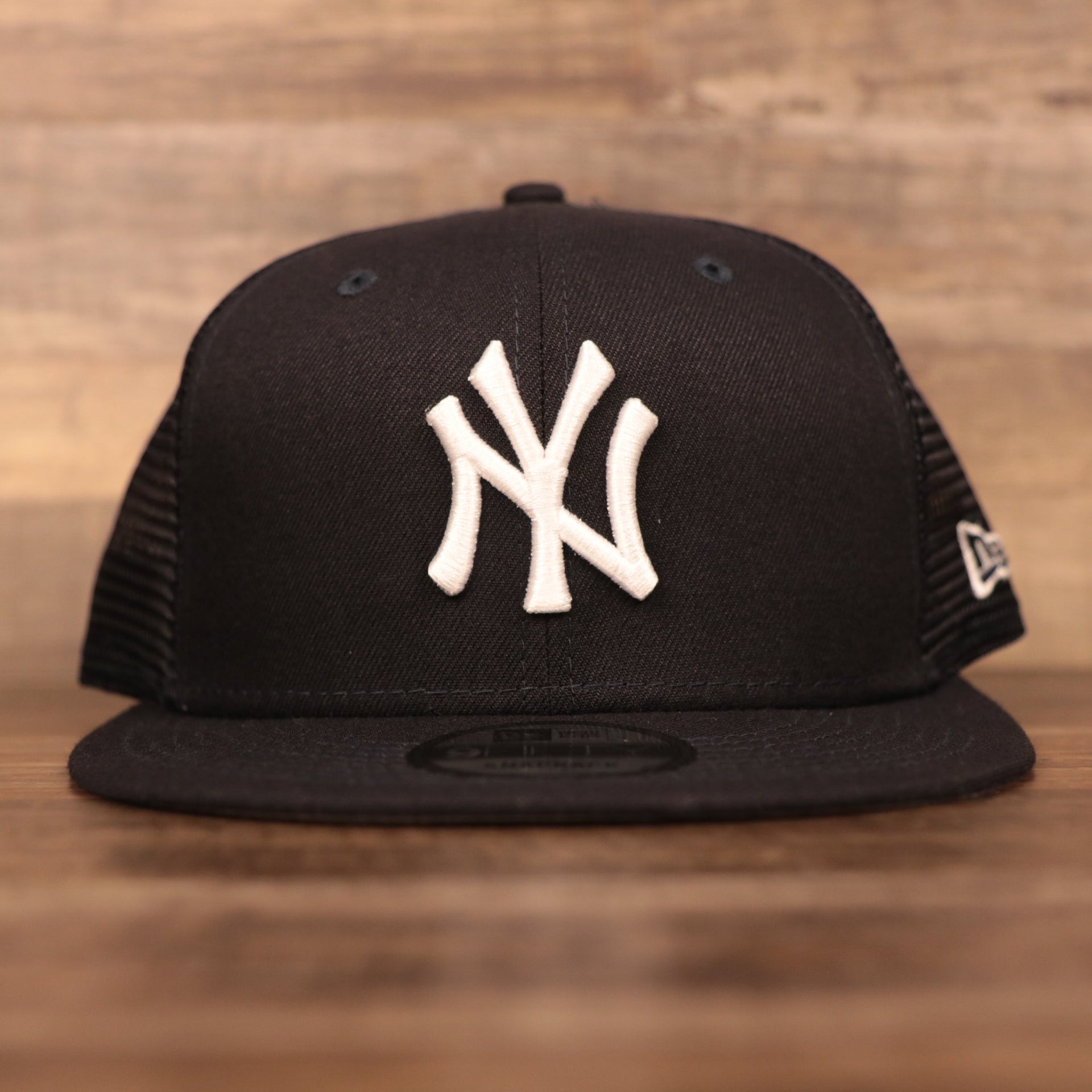 The logo of the New York Yankees on the front side of the navy New Era trucker hat.