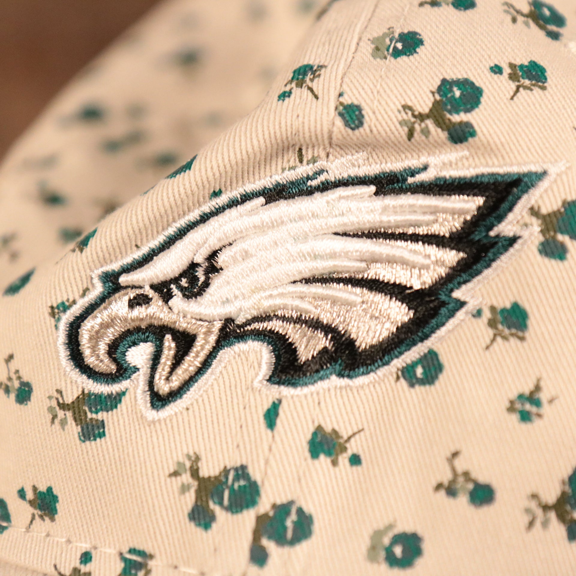 The Philadelphia Eagles logo on the front side of the cream youth micro floral hat.