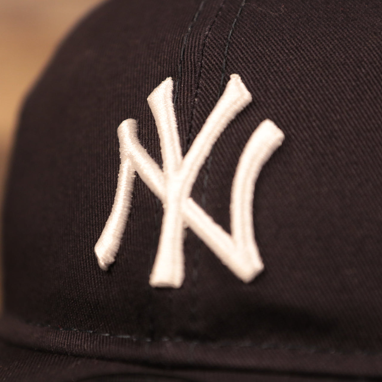The white New York Yankees logo patch on the front side of the New Era infant dad hat.