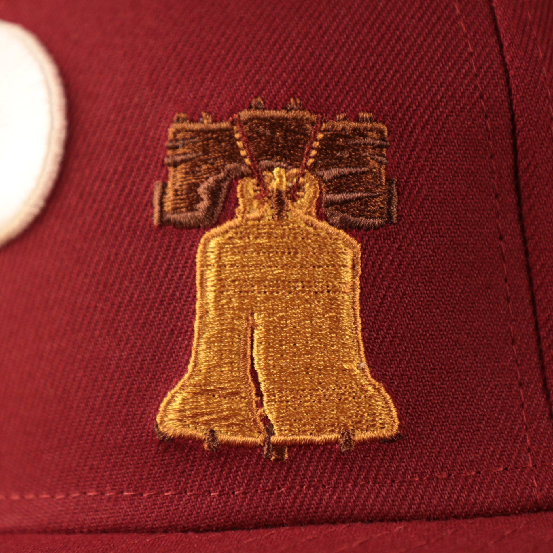 A close up shot of the Liberty Bell patch on the front side of the maroon Phillies 1980 World Series gray bottom brim 59fifty all over fitted hat by New Era.