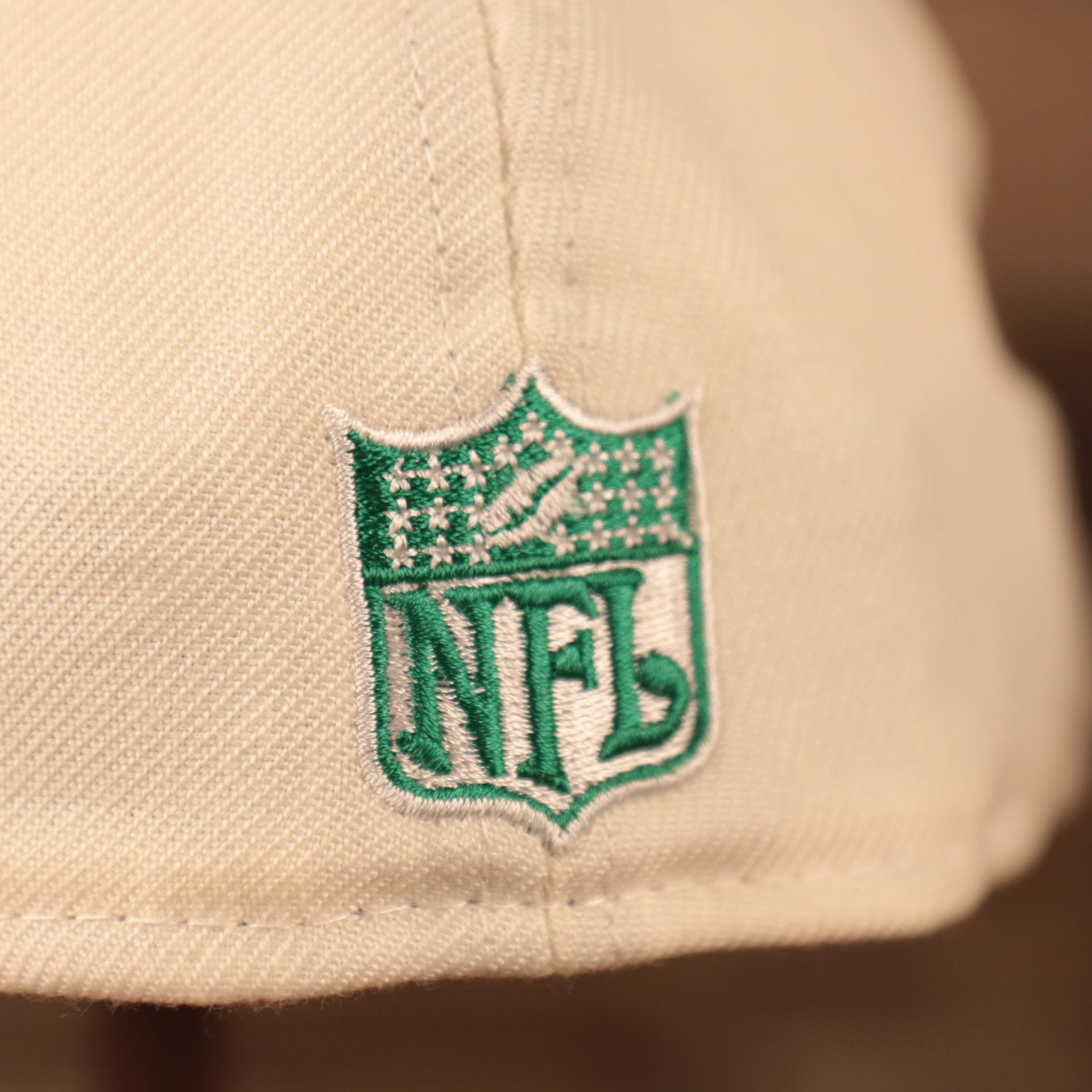 A close up shot of the green NFL logo patch on the backside of the cream Philadelphia Eagles gray bottom brim 59fifty fitted hat by New Era.