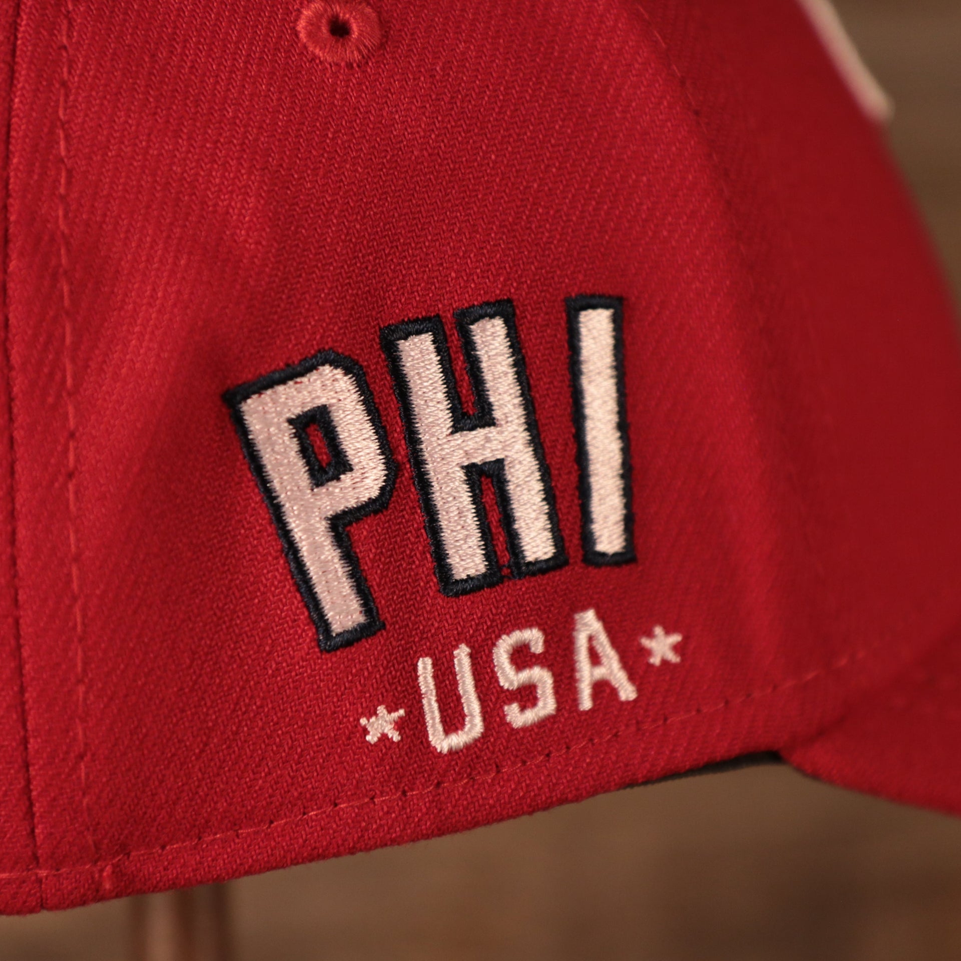 A closeup shot of the PHI USA patch on the wearer's right side of the red MLB fourth of July 2021 Philadelphia Phillies 39thirty flexfit hat.